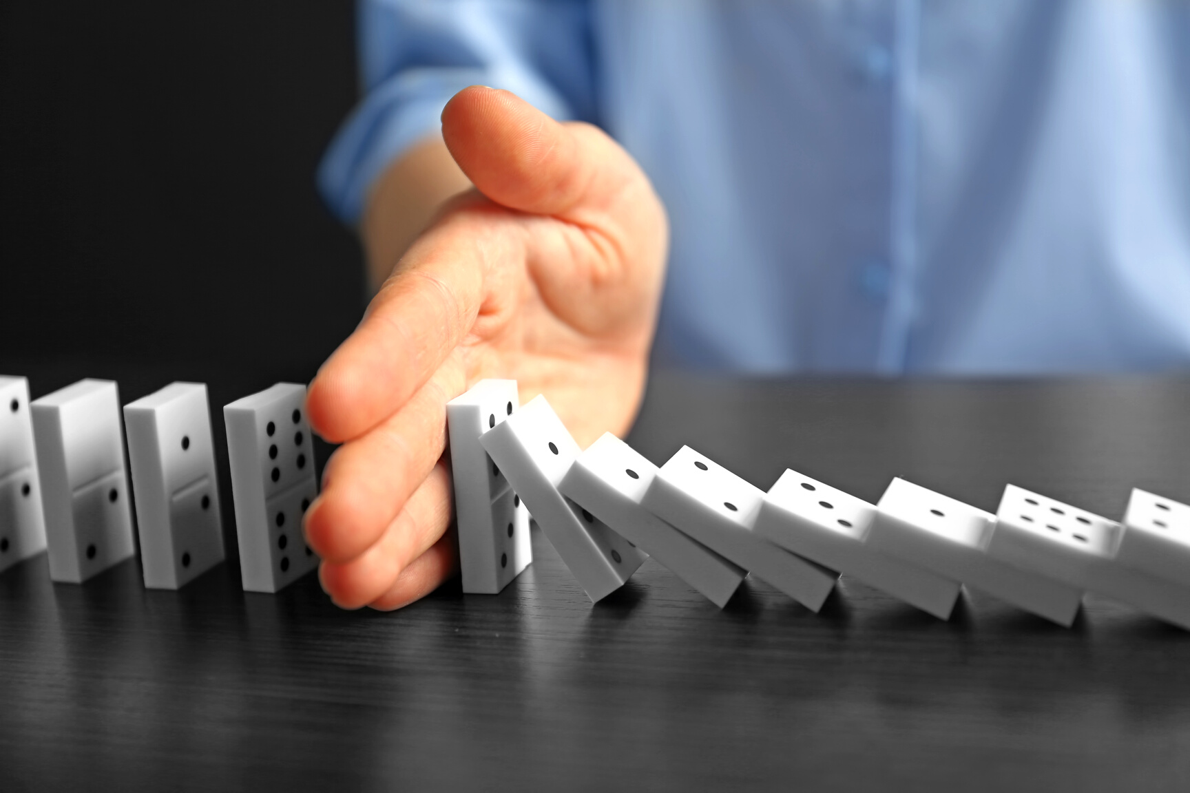 Person Stopping Domino From Falling